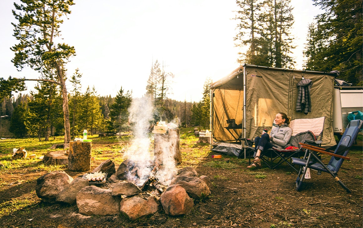 a woman by a tent near a campfire